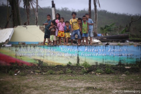 パグナミタン村の子供たち。塀には「幼稚園から高校までの教育が国の将来のリーダーを育てる」と書かれています。
